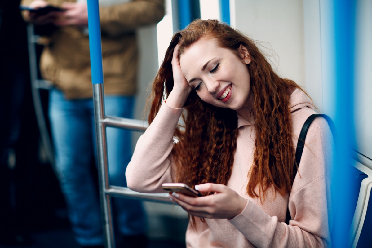 Positive redhead young female with mobile phone in subway train