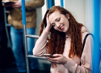 Positive redhead young female with mobile phone in subway train