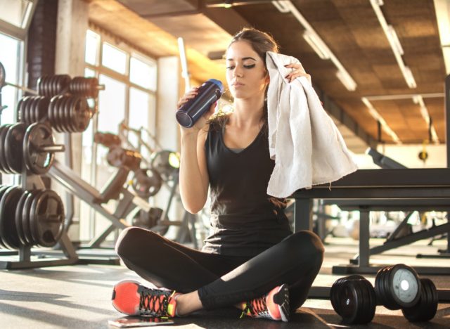 Young woman drinking water and taking a break after workout in gym,