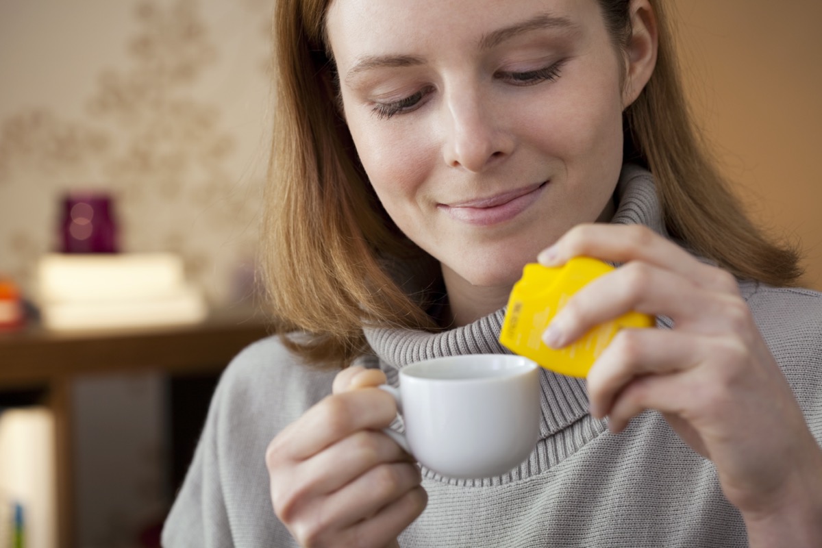 A woman adds artificial sweetener to her coffee cup.