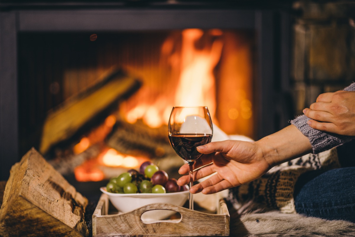 Woman in woollen socks taking a glass of red wine relaxing by the cozy fireplace