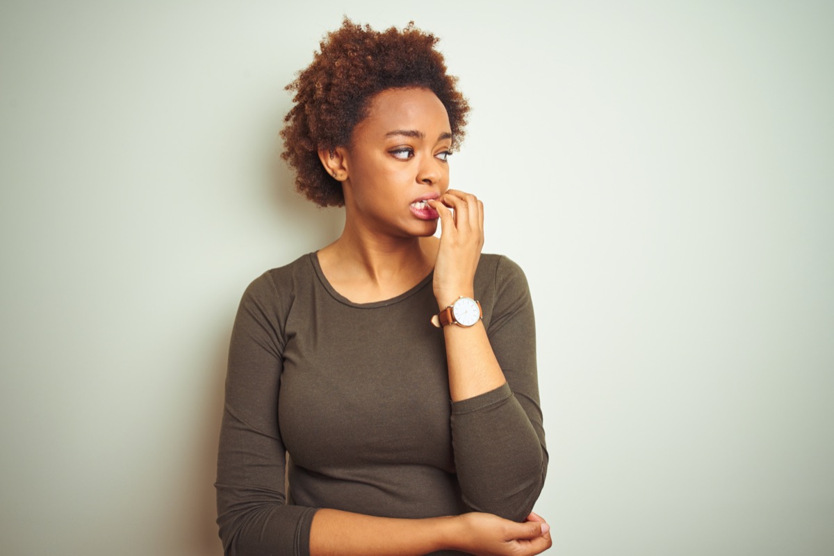 woman with afro hair over isolated background looking stressed and nervous with hands on mouth biting nails
