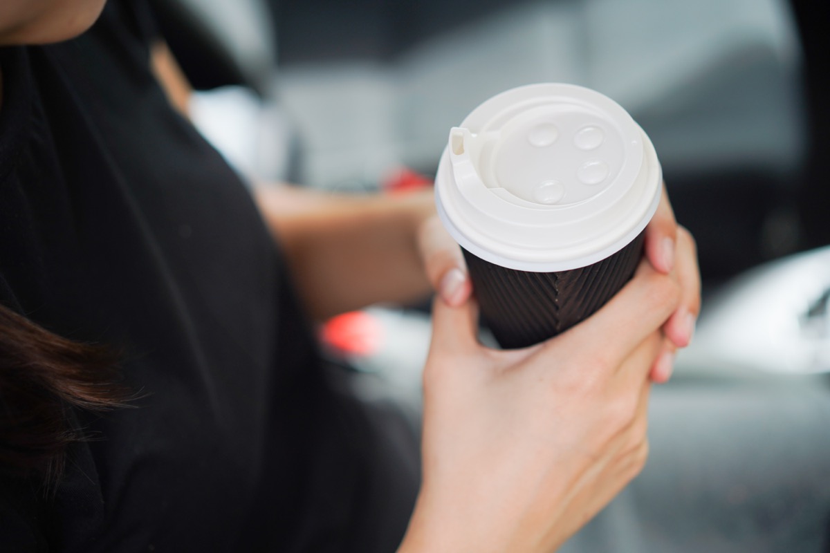 Young woman holding take out coffee cup in car