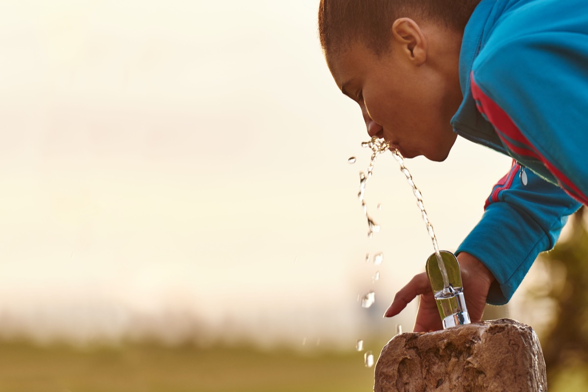 Close up image of a young mixed race girl busy drinking water from a fixed water fountain station with beautiful copy space