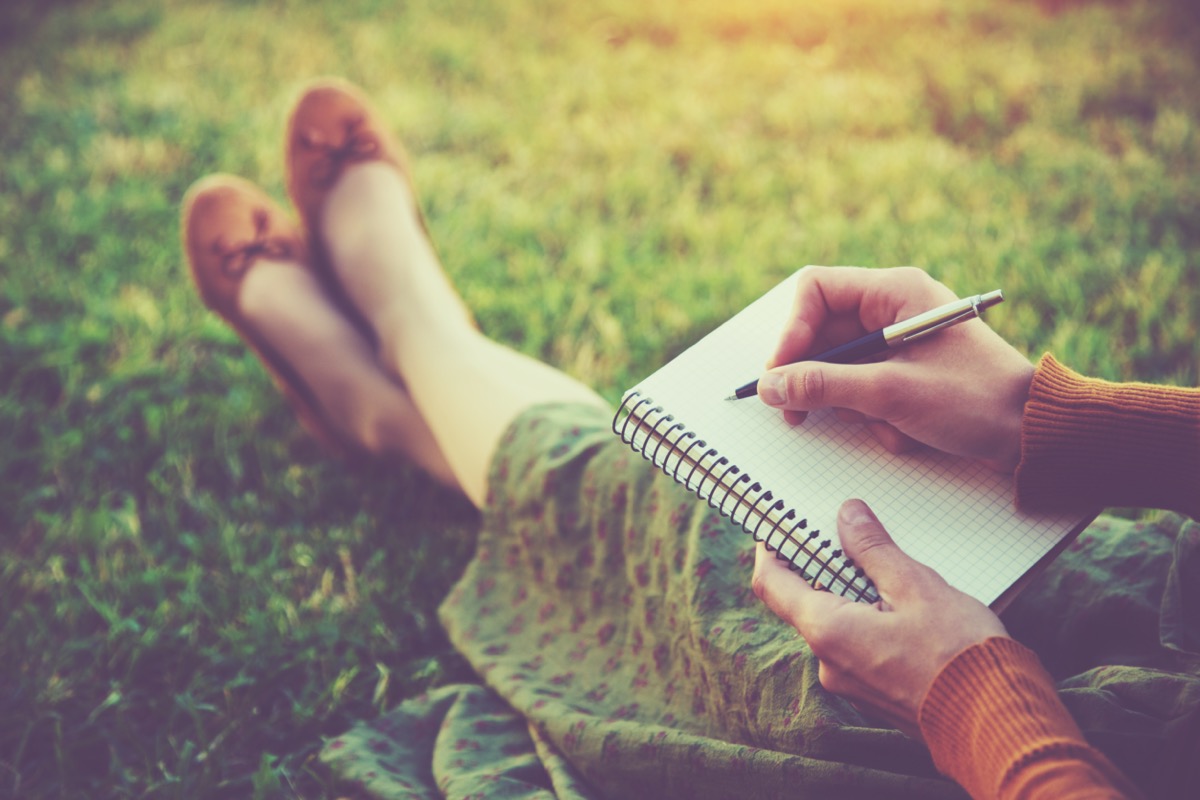 woman sitting in grass writing in journal