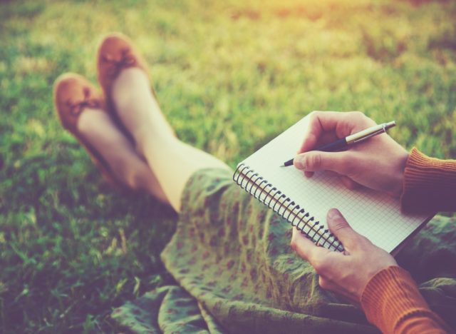 woman sitting in grass writing in journal