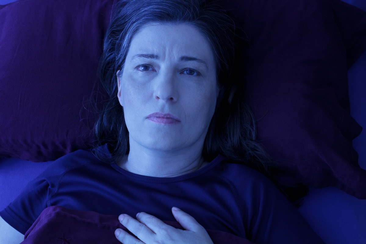 Middle aged woman lying awake in her bed at night, worrying because of an uncomfortable pressure in her chest and an irregular heartbeat