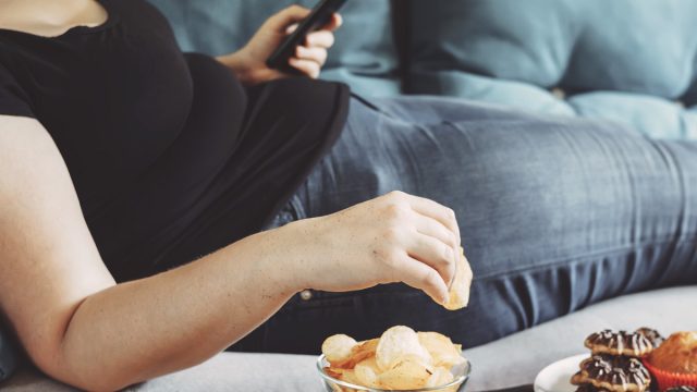 Woman emotional eating chips on couch scrolling through phone