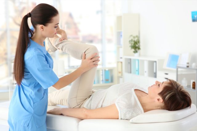 Female orthopedist massaging middle-aged woman in clinic.