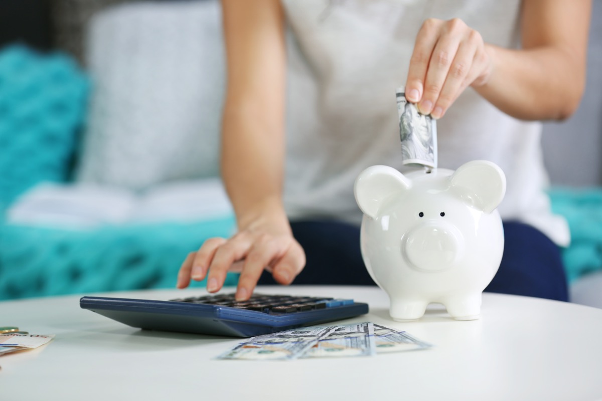 Female hand putting money into piggy bank and counting on calculator closeup