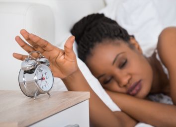 Woman Turning Off Alarm While Sleeping On Bed