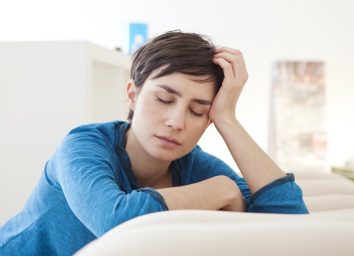 Tired woman with closed eyes leaning over coach at home