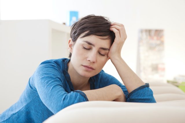 Tired woman with closed eyes leaning over coach at home