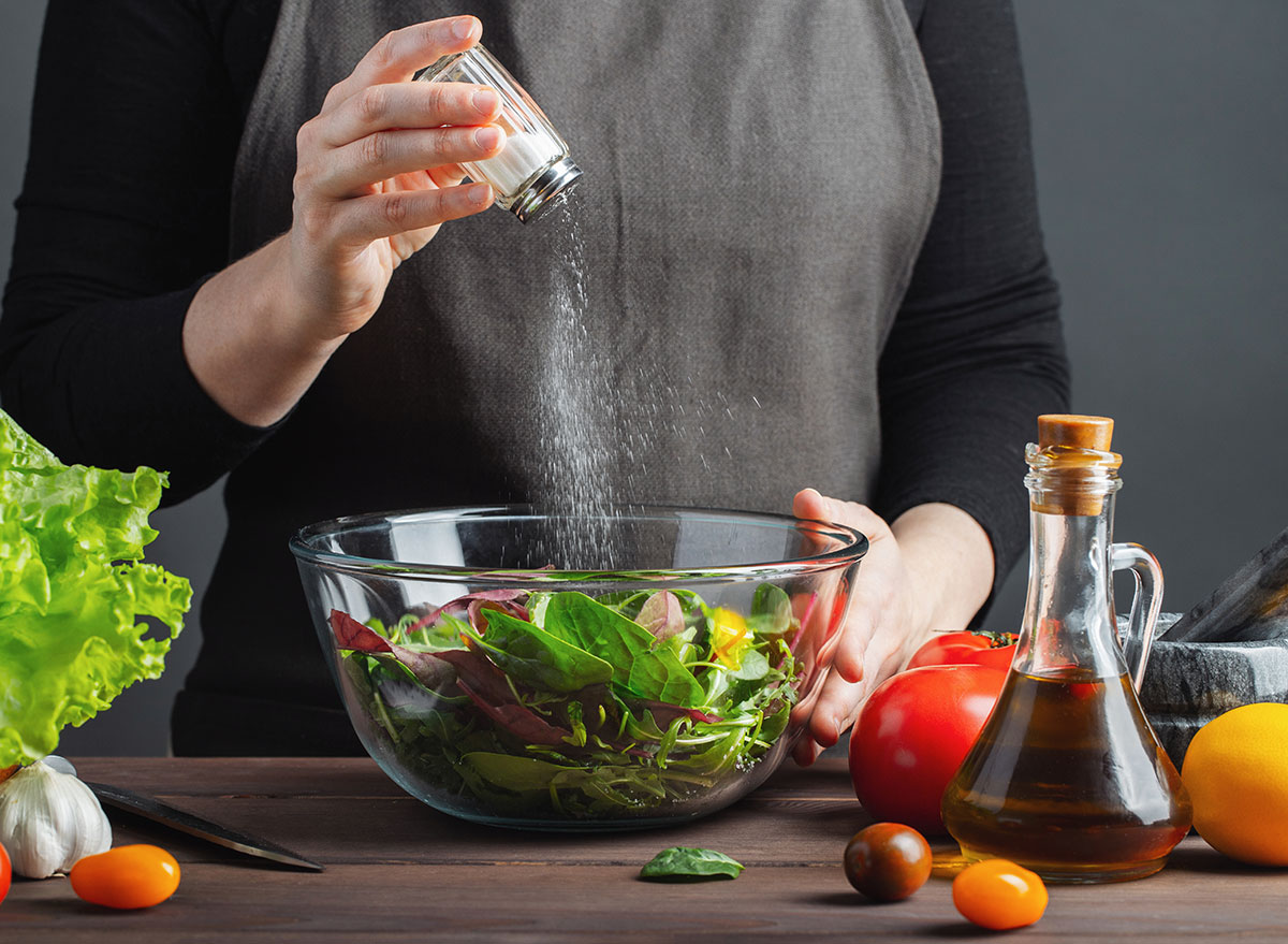 Women seasoning salad with salt