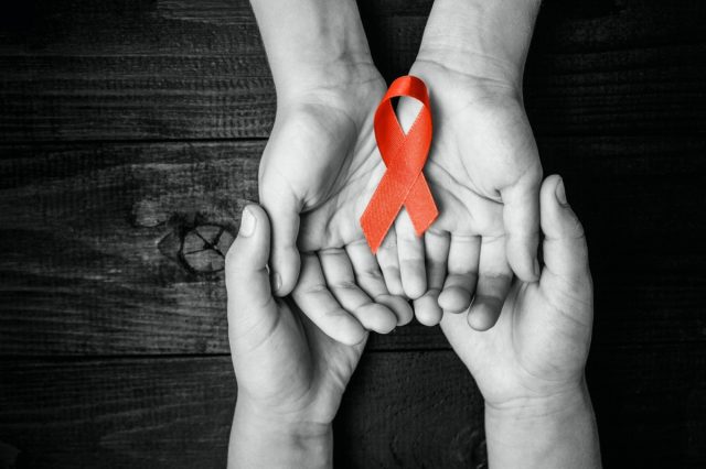 AID red ribbon in hand on a black wooden background, a symbol of the fight against HIV, AIDS and cancer