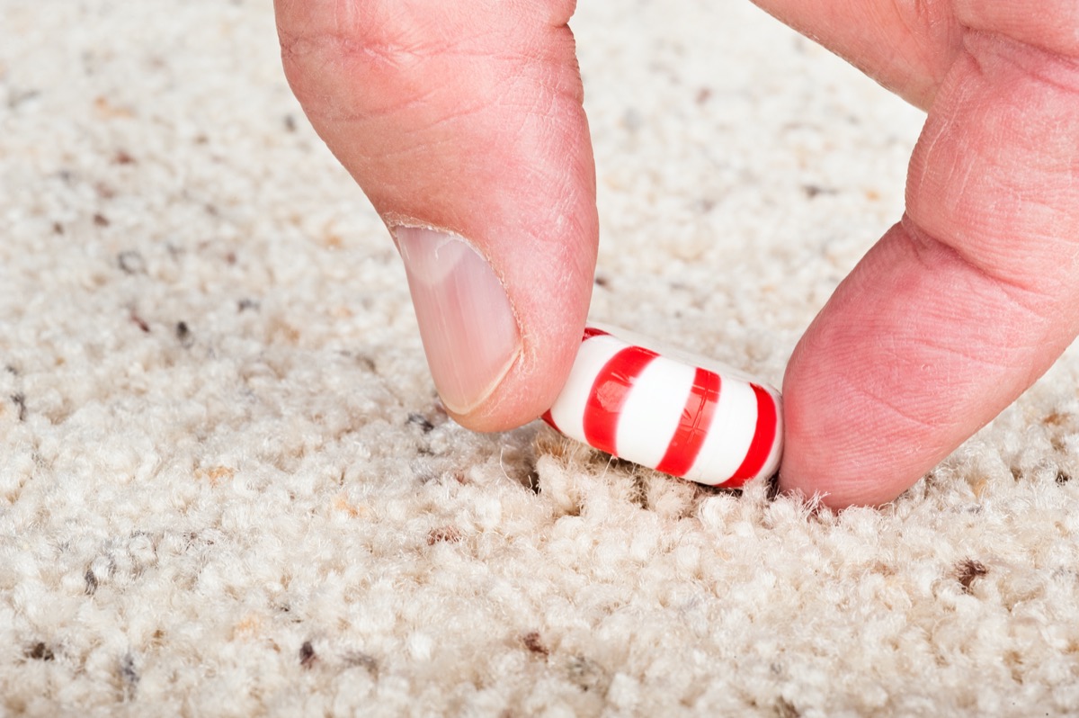 A person pulling a sticky candy mint off the carpet.