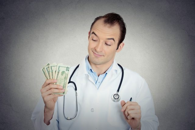 Portrait of a health care professional, male doctor holding, protecting his money dollars in hand