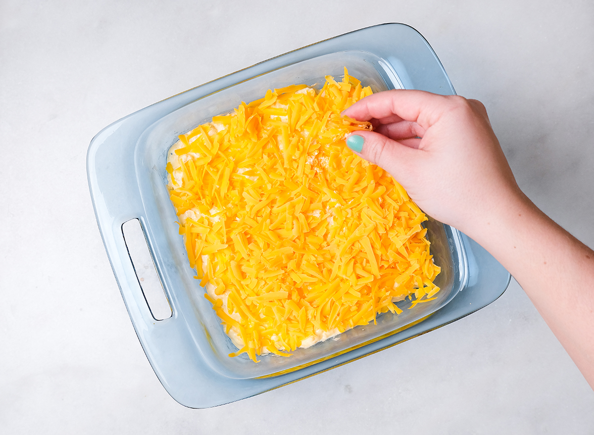 sprinkling shredded cheese on cauliflower mac and cheese in a casserole dish