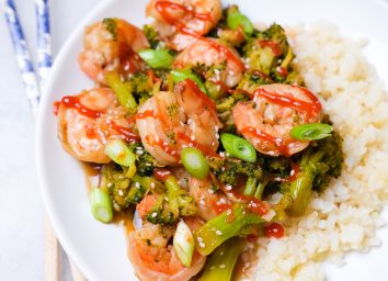 shrimp and broccoli with cauliflower rice sprinkled with sesame seeds green onions and sriracha