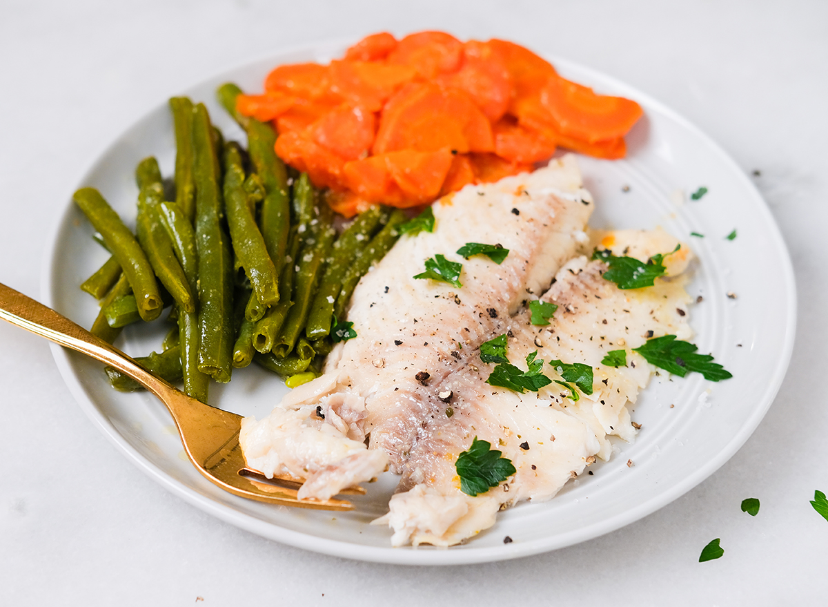 cooked tilapia with vegetables on a plate garnished with parsley