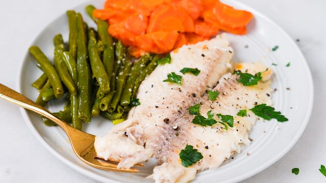 cooked tilapia with vegetables on a plate garnished with parsley