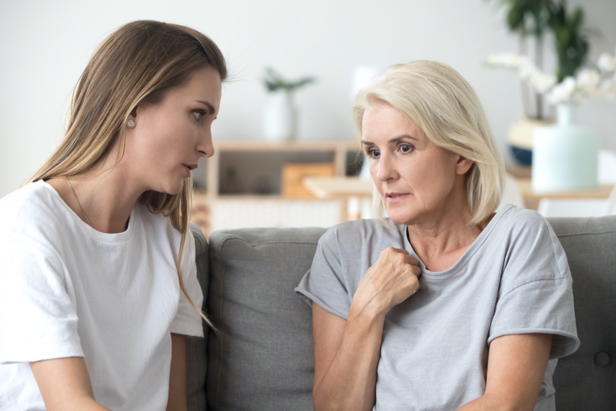 Concerned aged mother and adult daughter sit on couch having serious conversation