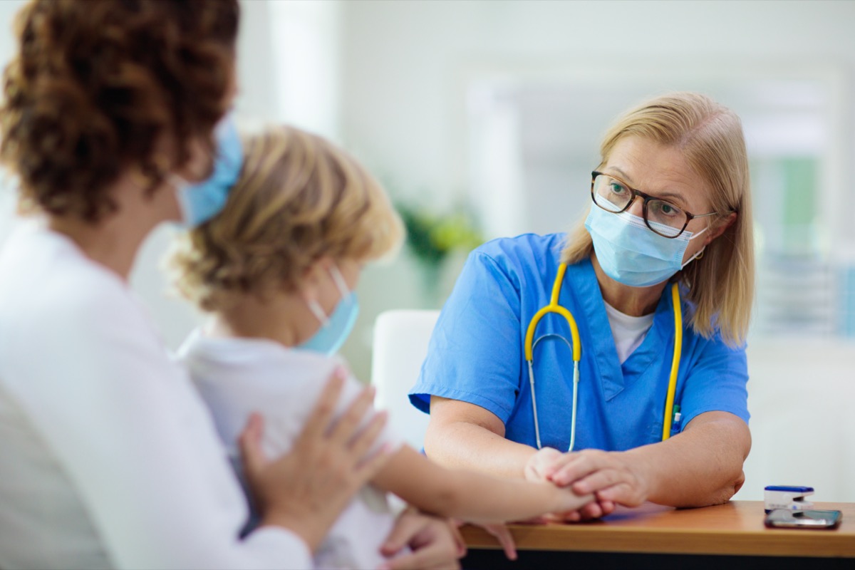 Pediatrician doctor examining sick child in face mask.