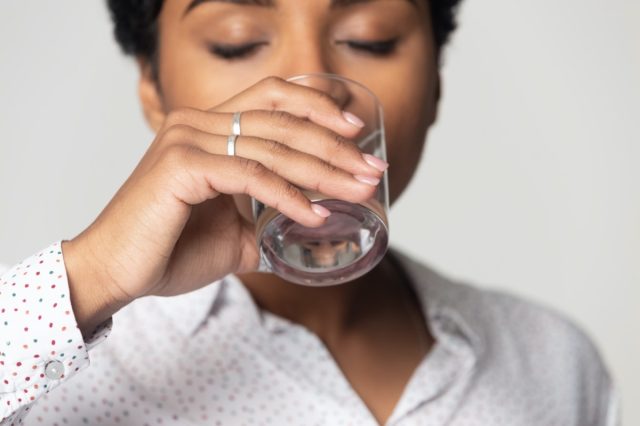 z zamkniętymi oczami pije czystą wodę mineralną z bliska, młoda kobieta trzyma szklankę