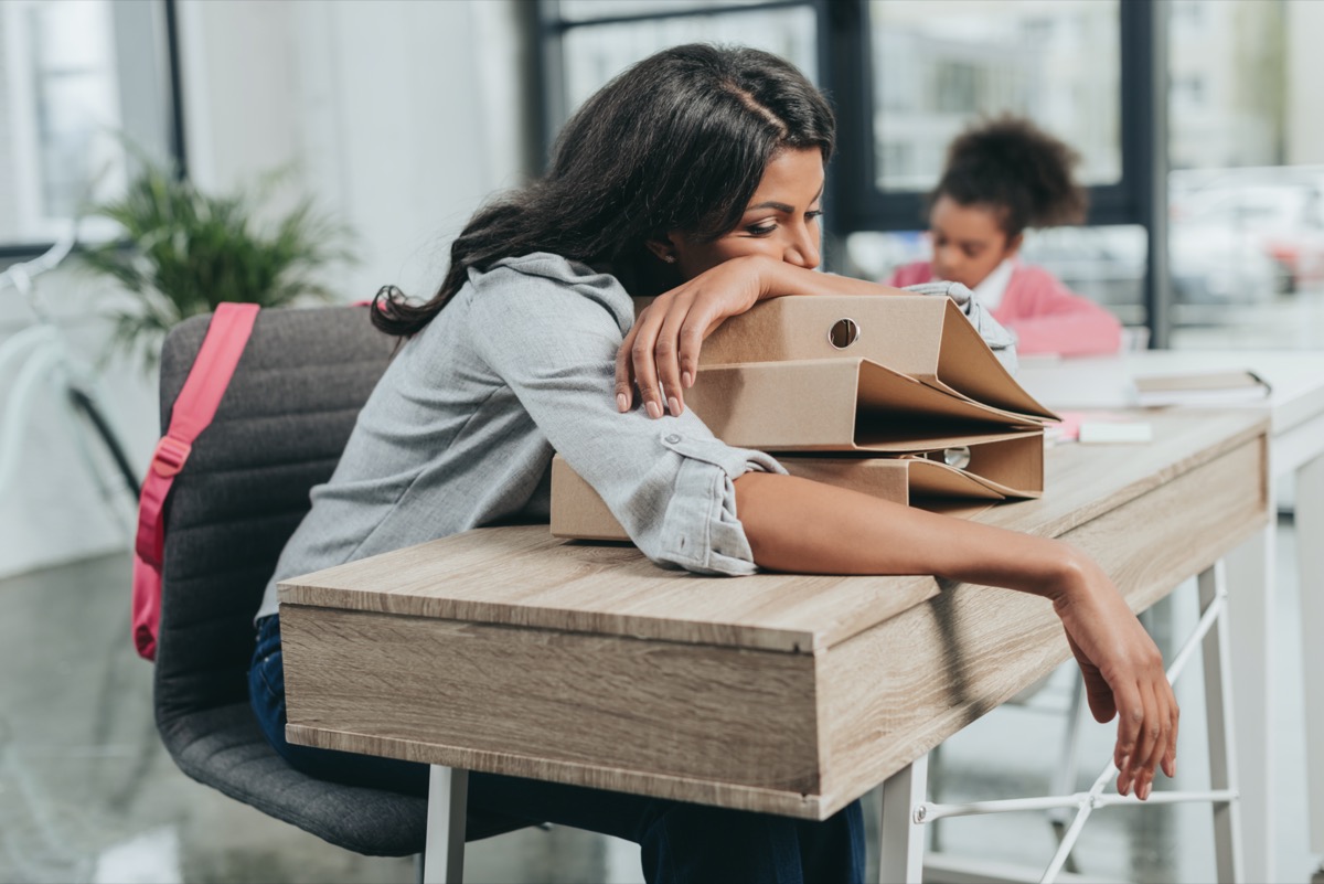 portrait of tired businesswoman lying on folders at workplace with daughter behind