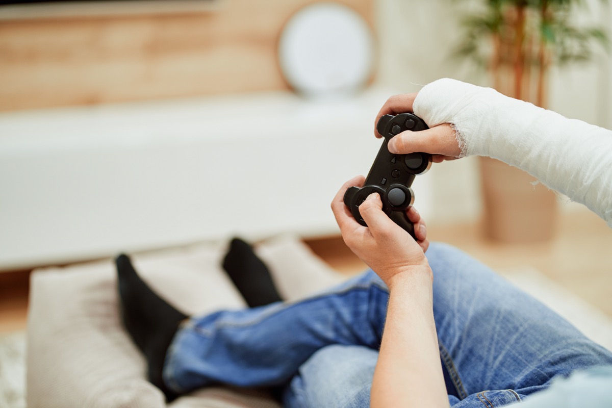 Man with broken arm in plaster cast holding controller and playing in videogame in front of TV.