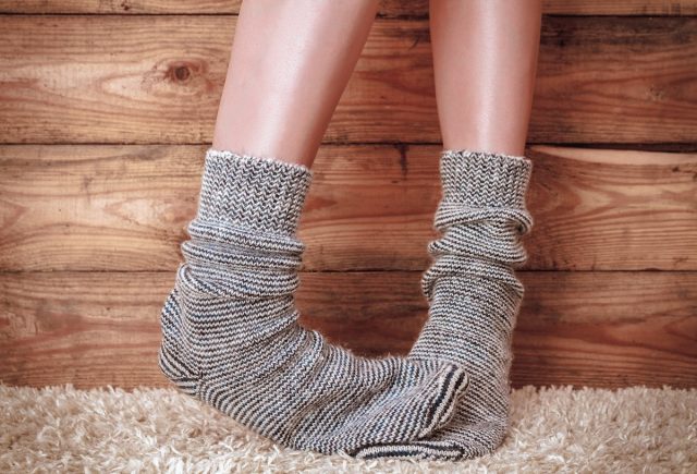 Legs of a woman in gray socks on the carpet on the wooden background
