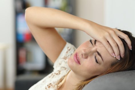 woman in a couch with headache and a hand on forehead