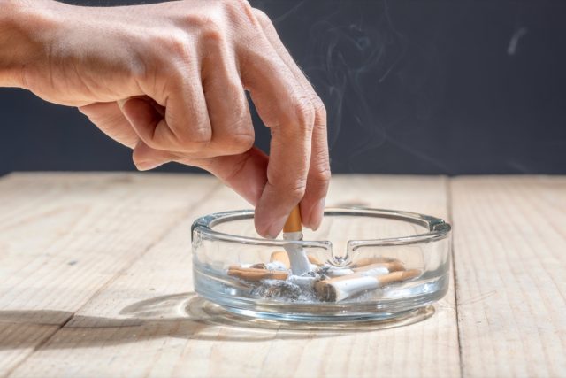 A hand-extinguished cigarette in a transparent ashtray on a wooden table