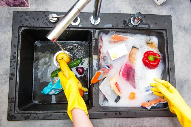 hands in yellow gloves are washing food products to get rid of bacteria or virus
