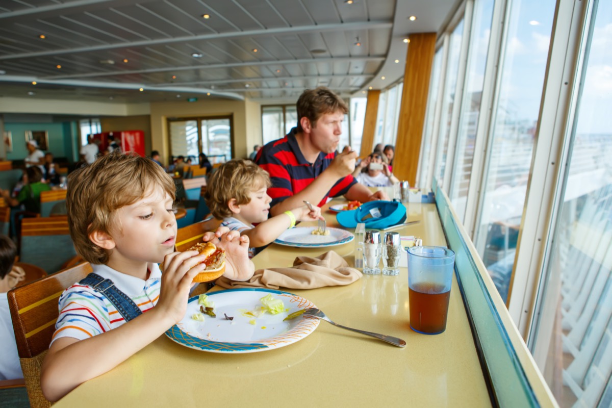 Two preschool kids and father boys eating pasta hamburger sitting in cafe on cruise ship