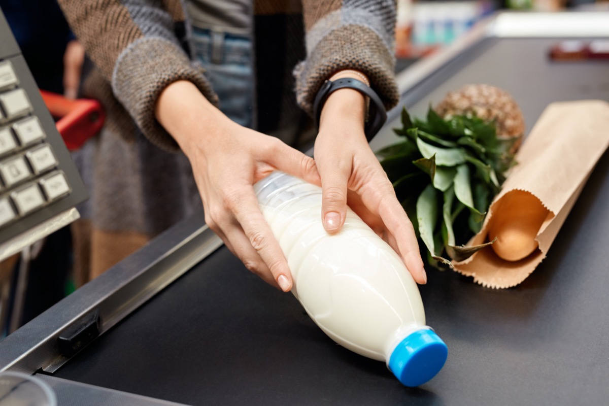 woman at the supermarket doing daily shoppings standing at cashier checkout counter putting milk on conveyor belt