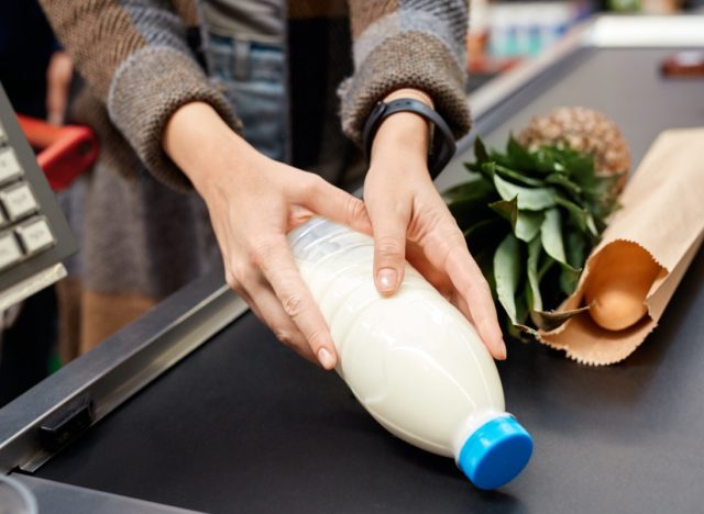 woman at the supermarket doing daily shoppings standing at cashier checkout counter putting milk on conveyor belt