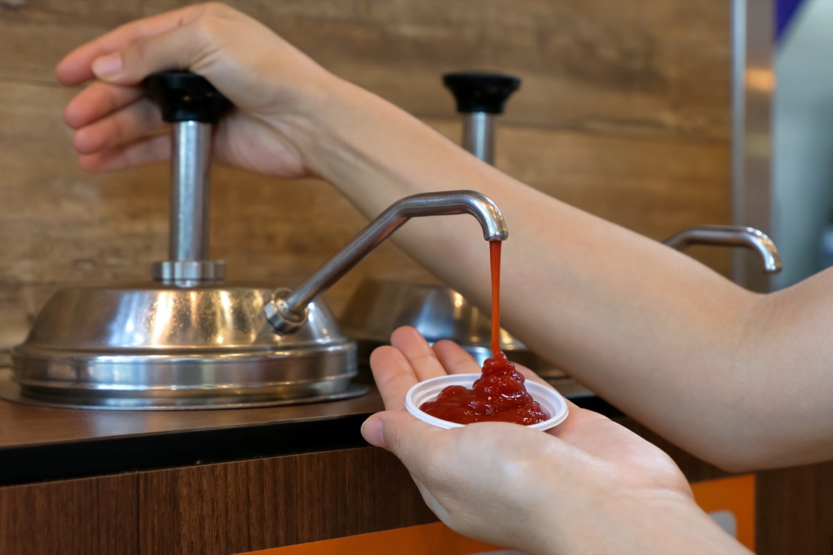 Hand pumping ketchup from sauce pump in to small plastic bowl in fast food restaurant.