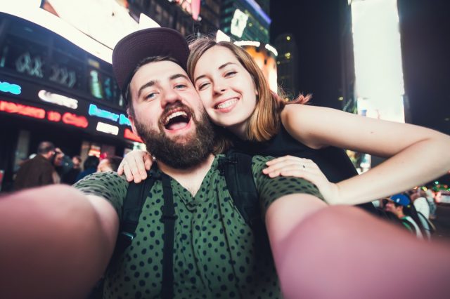 Happy dating couple in love taking selfie photo on Times Square in New York while travel across USA on honeymoon