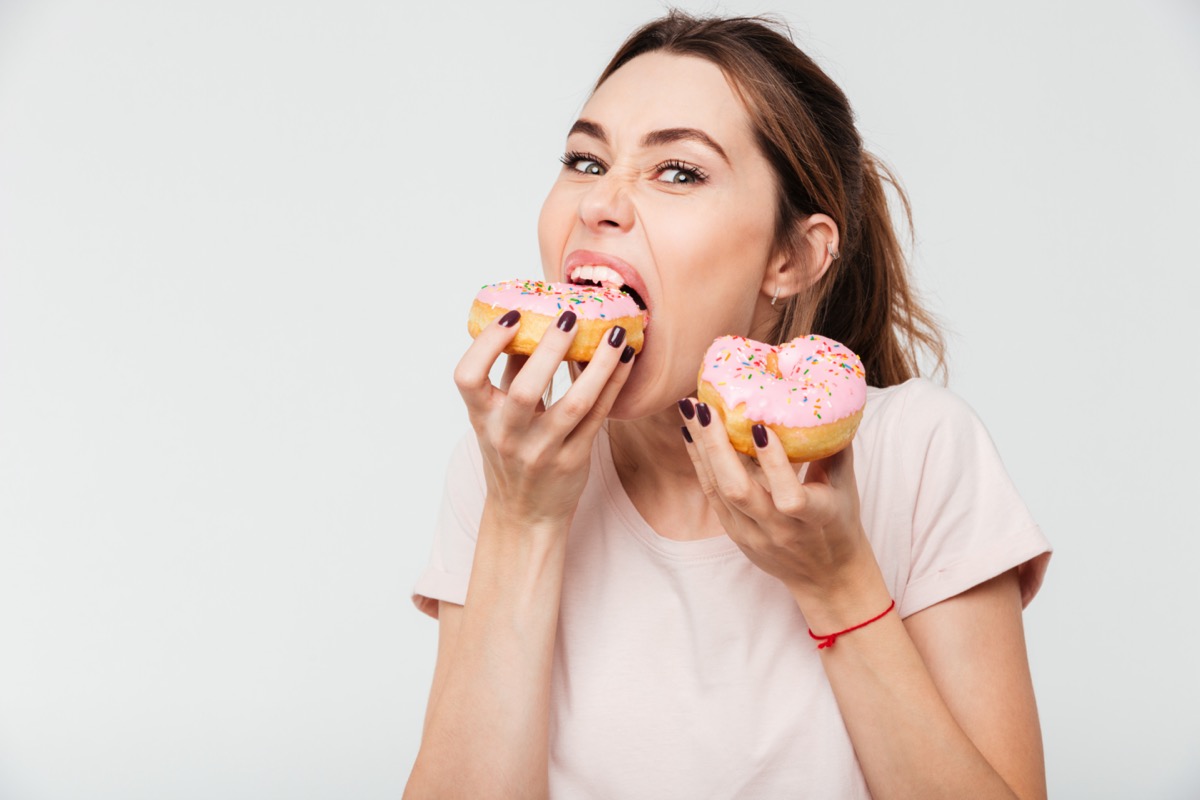 Close up portrait of a hungry greedy girl eating donuts