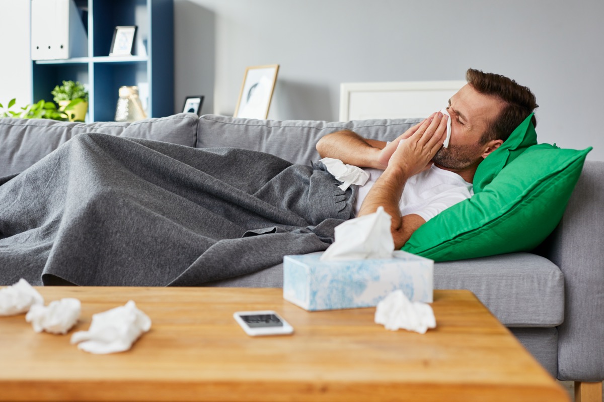 Sick man lying on sofa at home and blowing nose