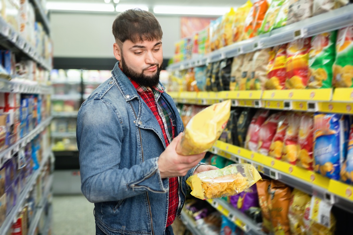 smiling glad friendly bearded guy choosing potato chips at grocery store
