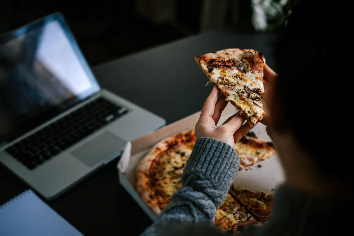 Eating pizza and social networking with a laptop.