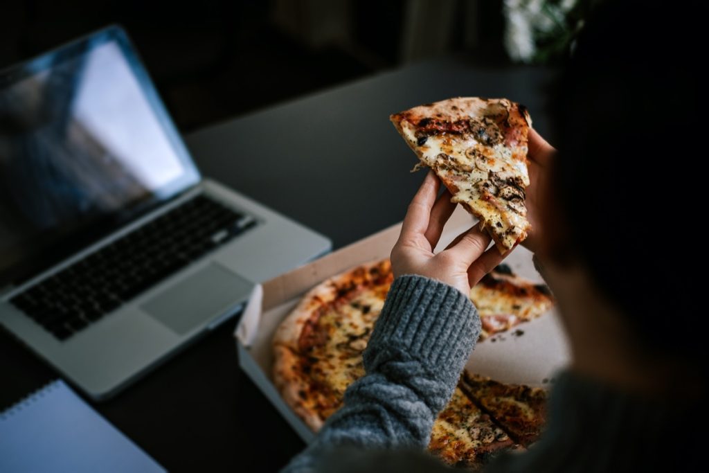Eating pizza and social networking with laptop.