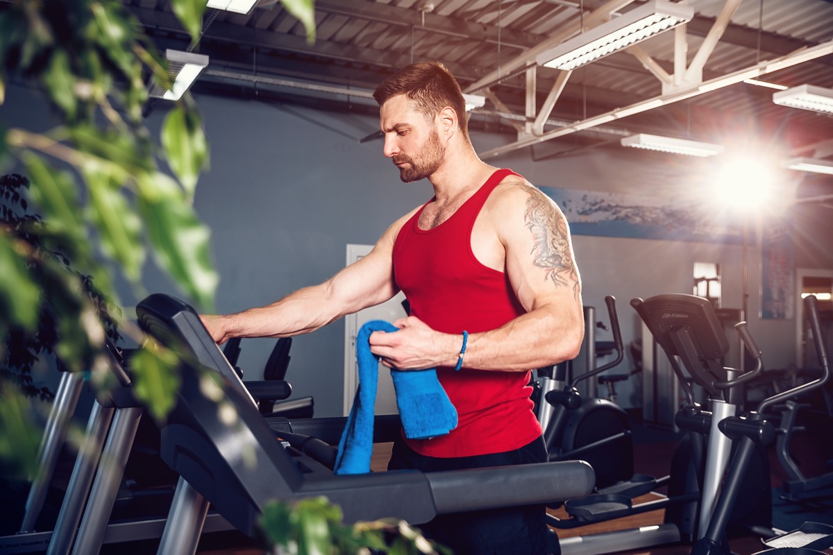 Man wiping his face with a towel beside a treadmill