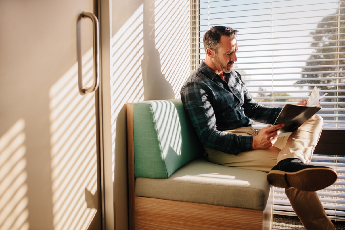 Mature male patient reading a book in the doctor's waiting room