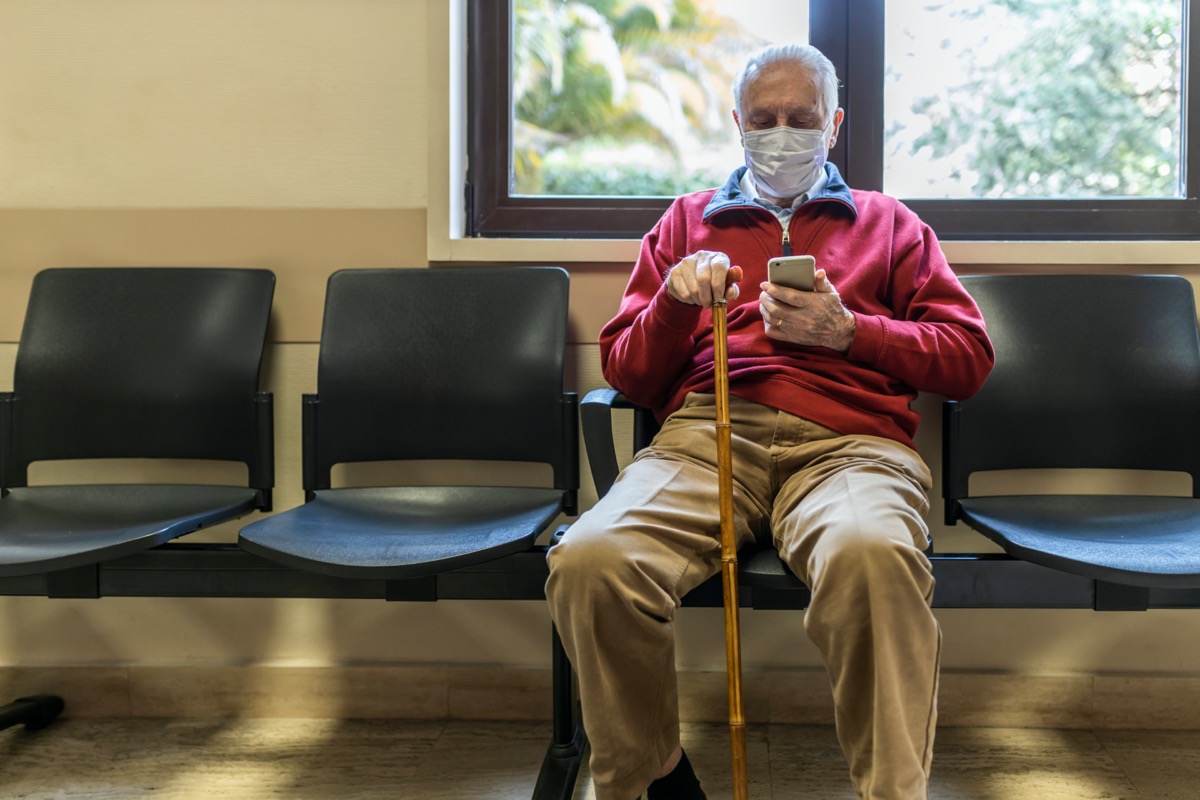 elderly man sitting at the doctor's office in a hospital with respirator and using his smart phone