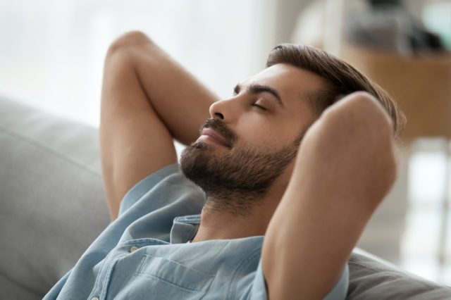 Relaxed happy young man resting having nap on comfortable couch breathing fresh air