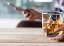 Man relaxing with bourbon whiskey drink alcoholic beverage in hand and using mobile smartphone