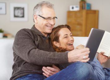 Affectionate middle-aged couple relaxing on a sofa together at home laughing at something on a tablet computer, natural and spontaneous